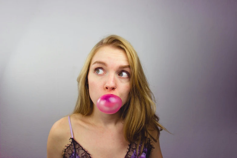 a woman is blowing her pink gum in front of her face