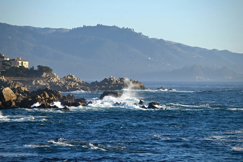 ocean waves splash in front of rocky shoreline and houses