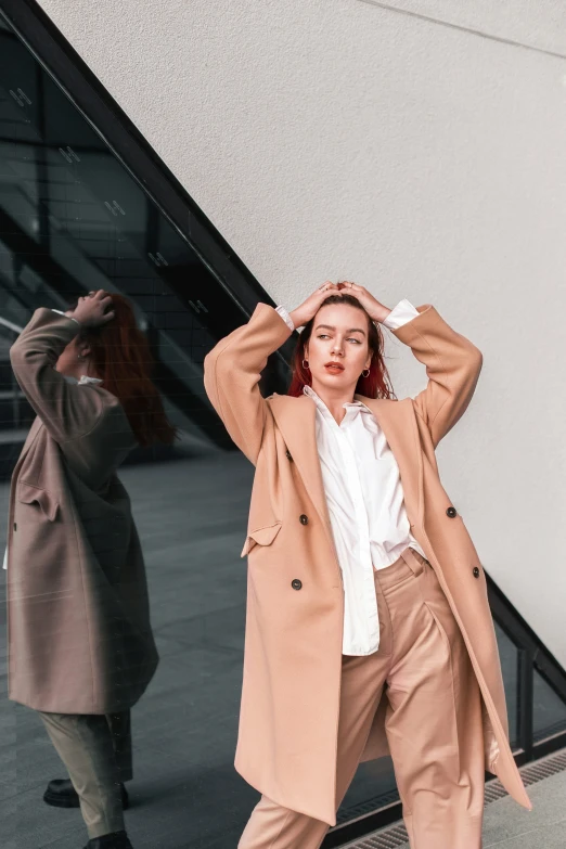 a woman in a tan coat posing against a white wall