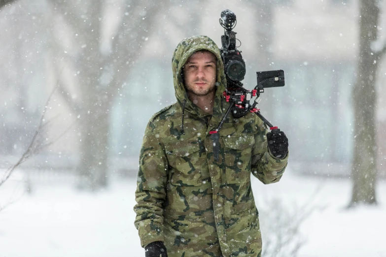 a man in a hoodie carrying a camera through the snow