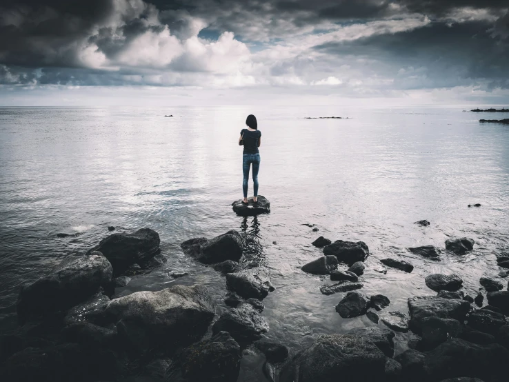 black and white po of a girl standing on rocks in the ocean