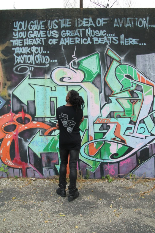 a  with dreadlocks is standing in front of a wall with graffiti