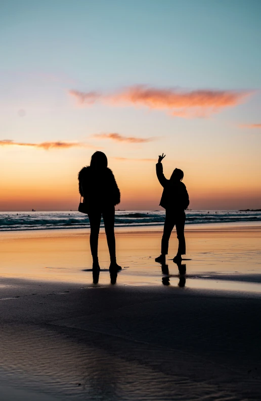 two people walking across a wet beach at sunset