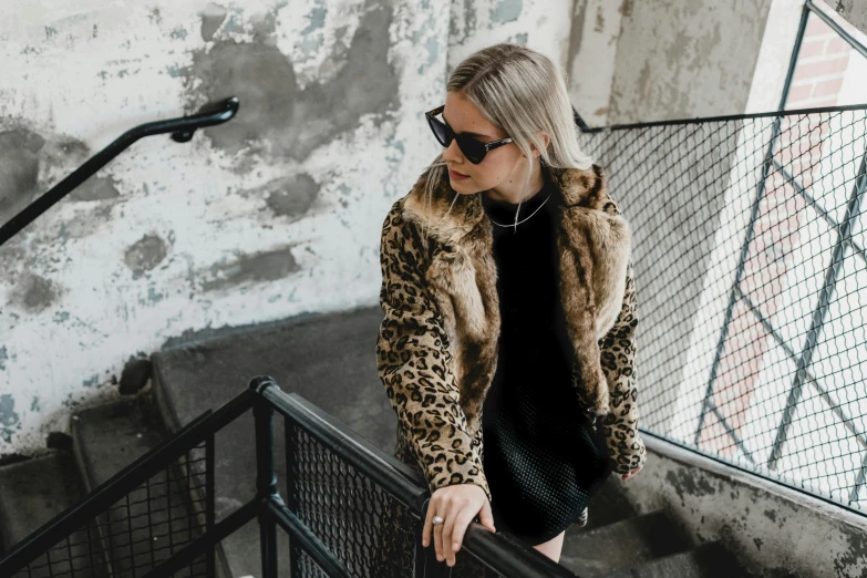 a woman wearing a fur coat and black dress walks along some stairs