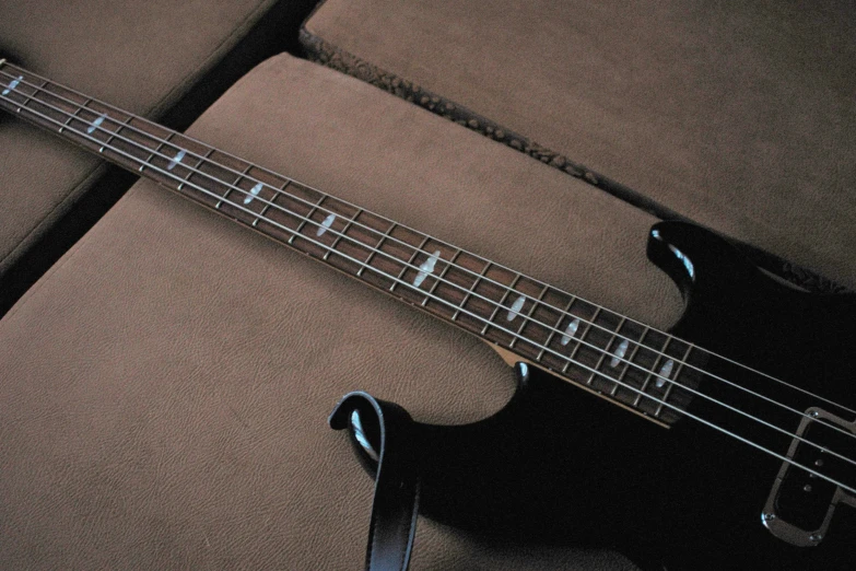 a black bass guitar with its neck up on a couch