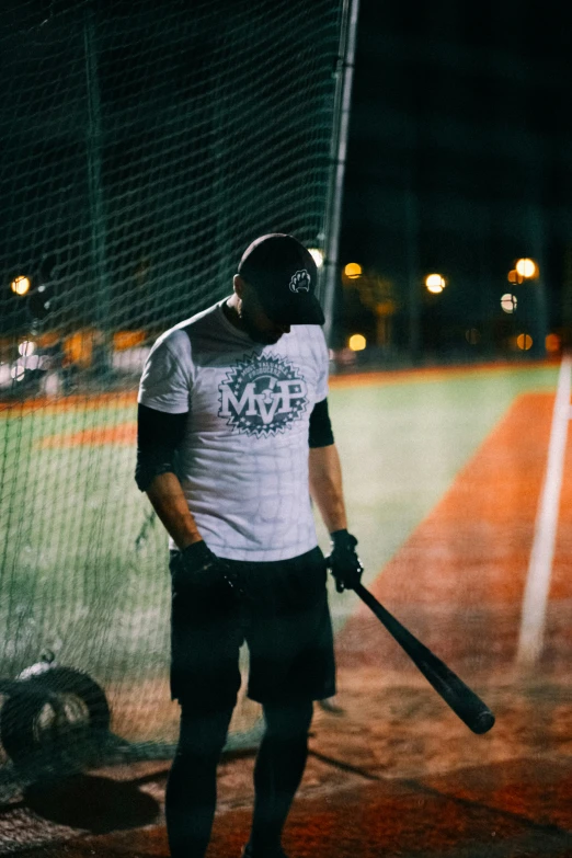 man carrying baseball bat and ball at night on the field