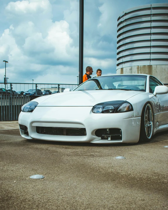 two men are sitting in the front of a white sports car