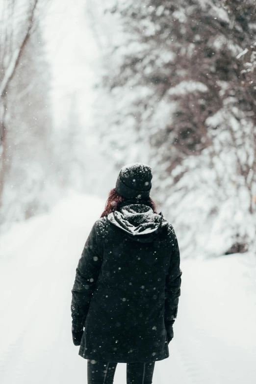 person in black jacket walking on snow path