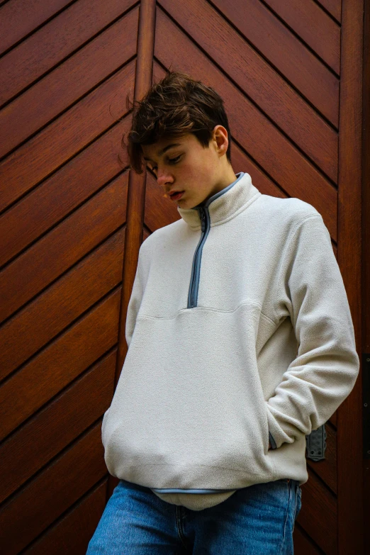 a boy in white sweatshirt and jeans stands against a brown door