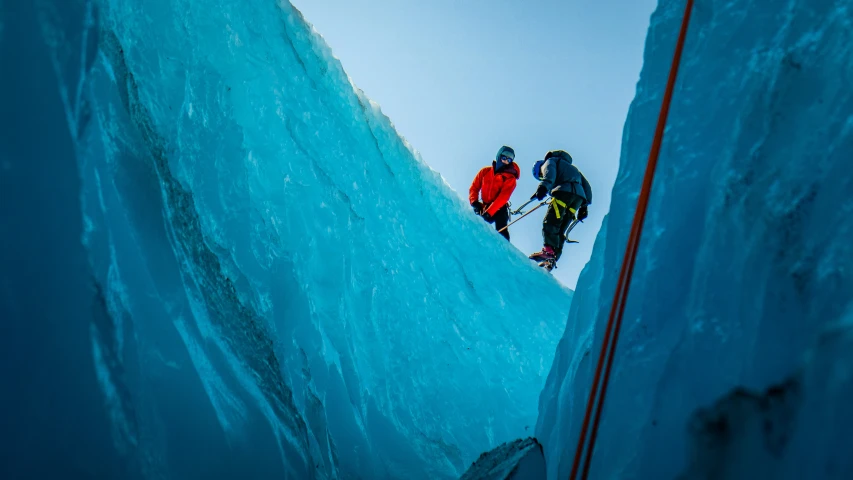 two men climbing up the side of a glacier