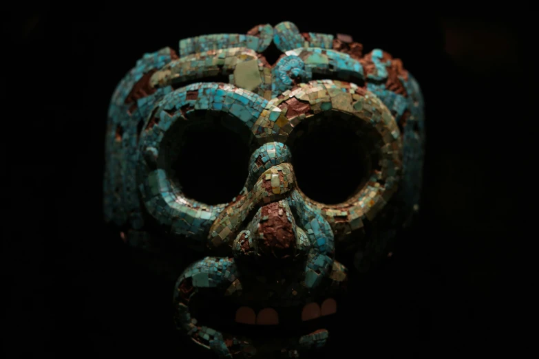 an ancient mask covered in mosaics sits on a black background