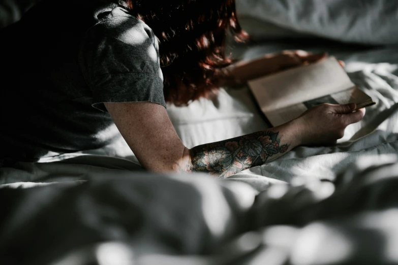 someone reading on their bed with tattoo sleeves