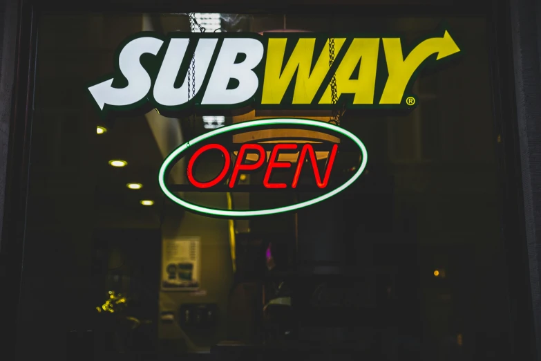 the front of sub way, which has a green neon sign in the window