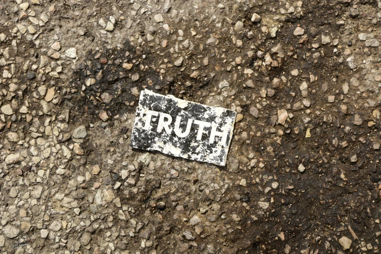 an old dirty white sign with a tag on it is on a dirt road