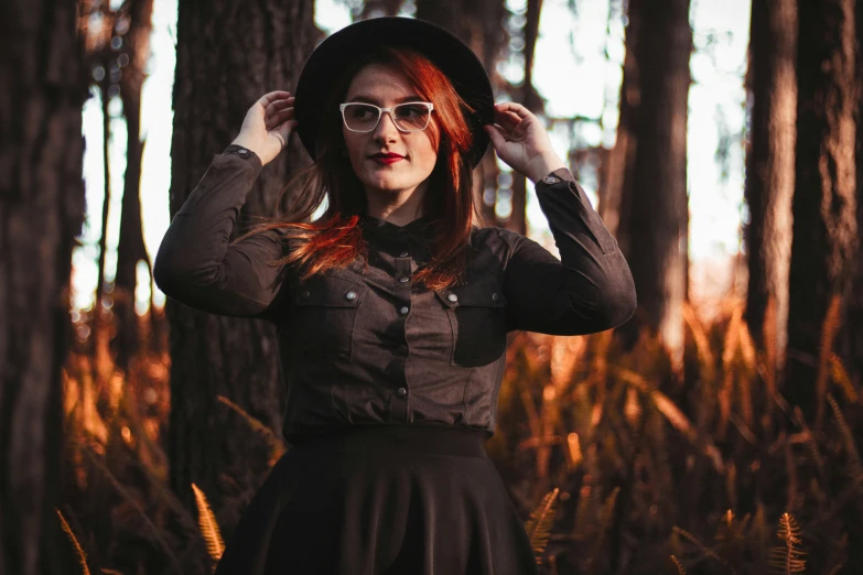red haired woman wearing sunglasses and a hat in a forest