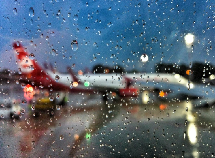 a blurry image of rain pouring on a passenger jet at an airport