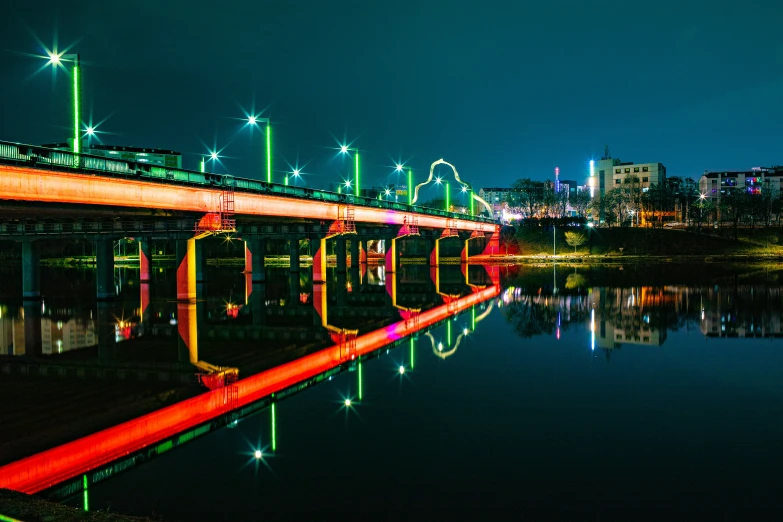 a lighted bridge going over a river in the city at night