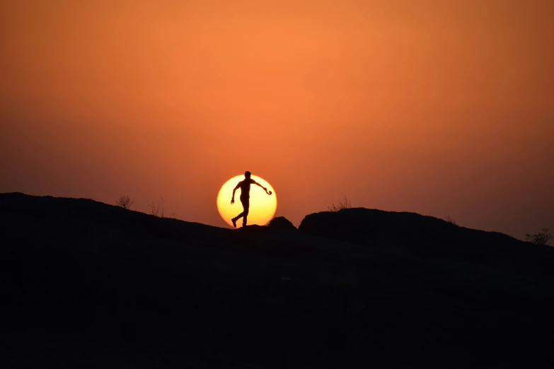 the man is walking across the hill toward the sun