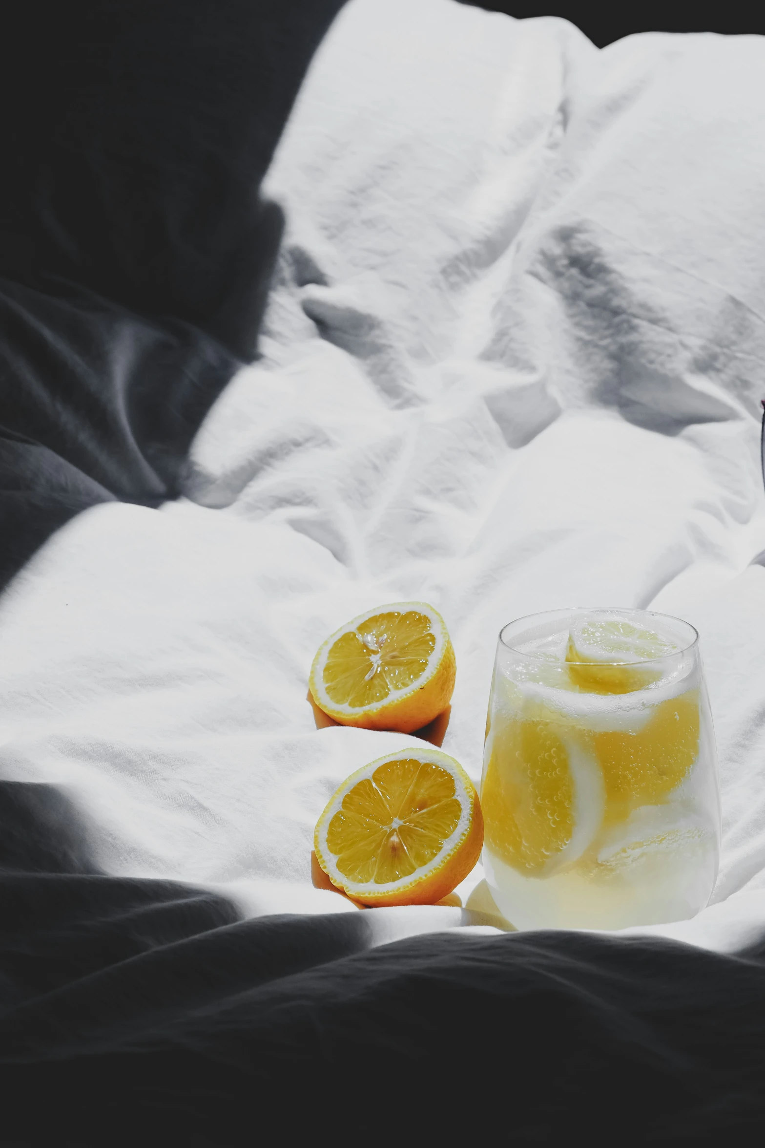 two glasses of water and sliced oranges sit on a bed