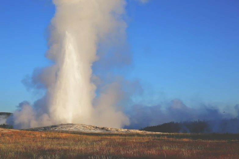 a geyser emitting steam on top of a hill