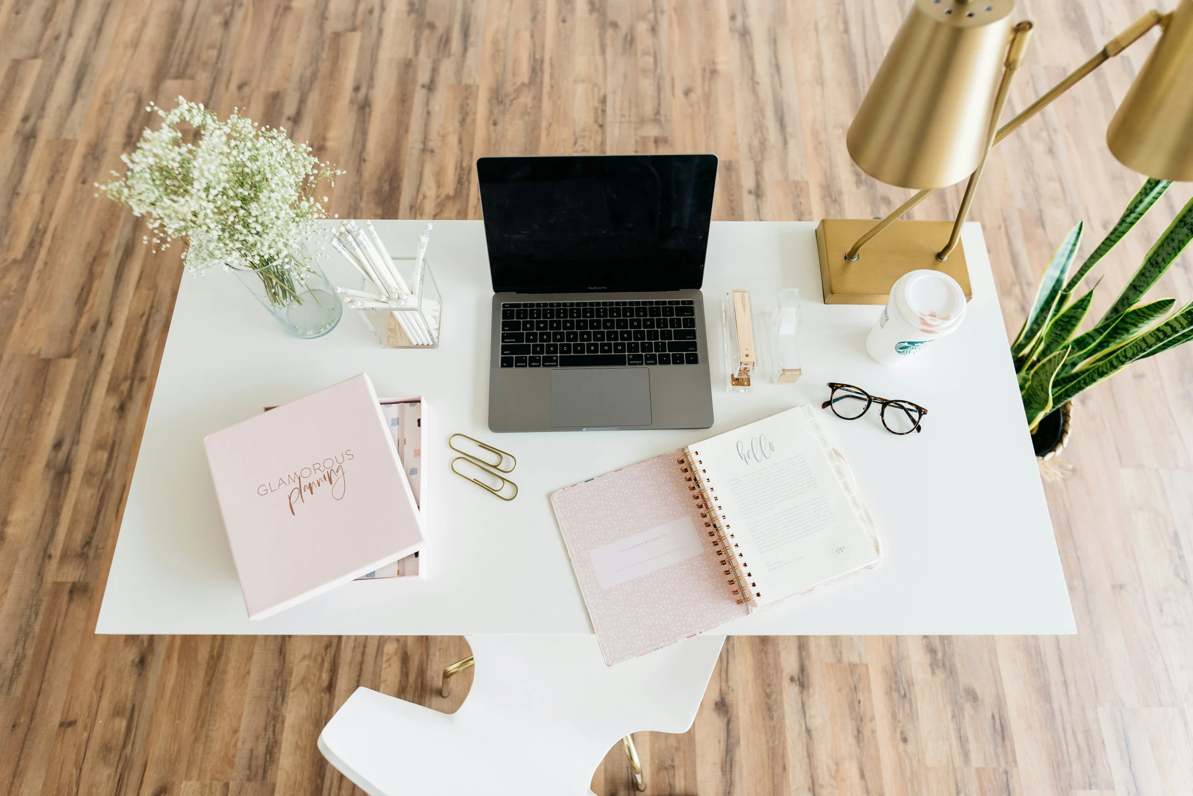 a desk with notebooks, pens, and flowers, along with an open laptop