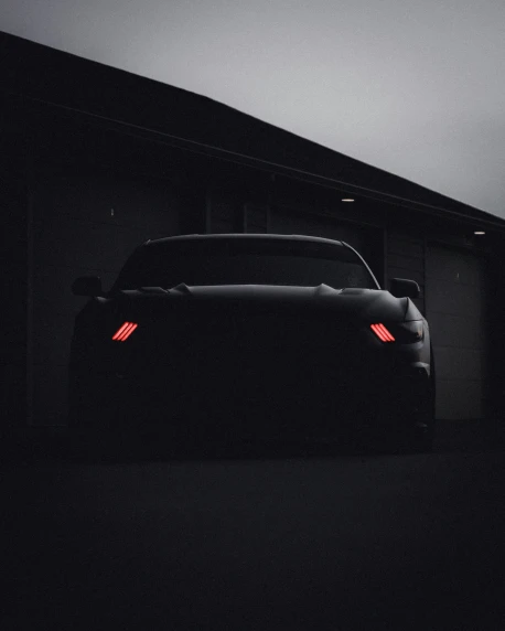 a black car sitting in the dark under some clouds