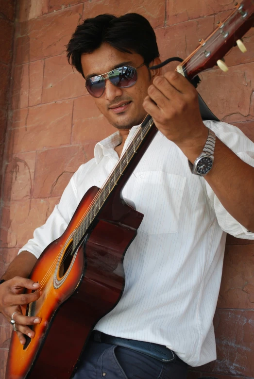 a man is playing guitar against a red brick wall