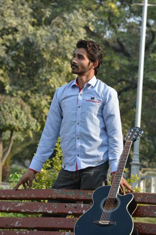 a man standing next to a guitar near a park bench