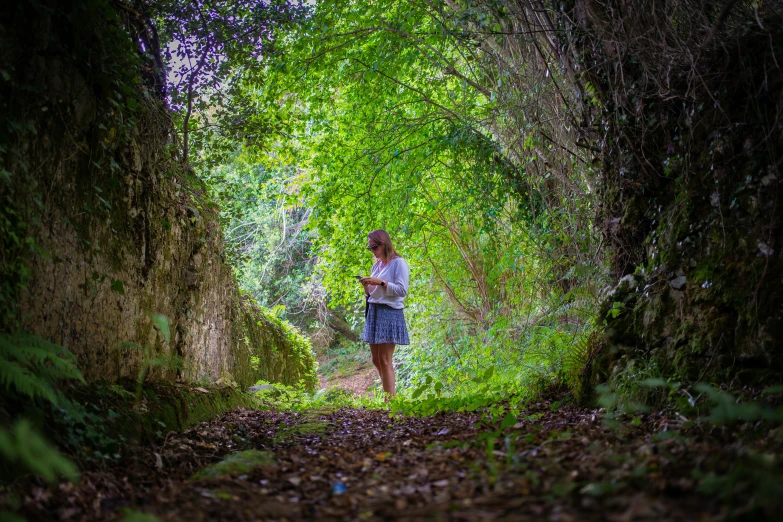 a woman stands in a tunnel of trees and leaves