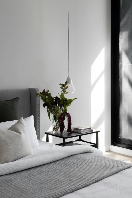 a bedroom with white walls and gray bedding and green plant