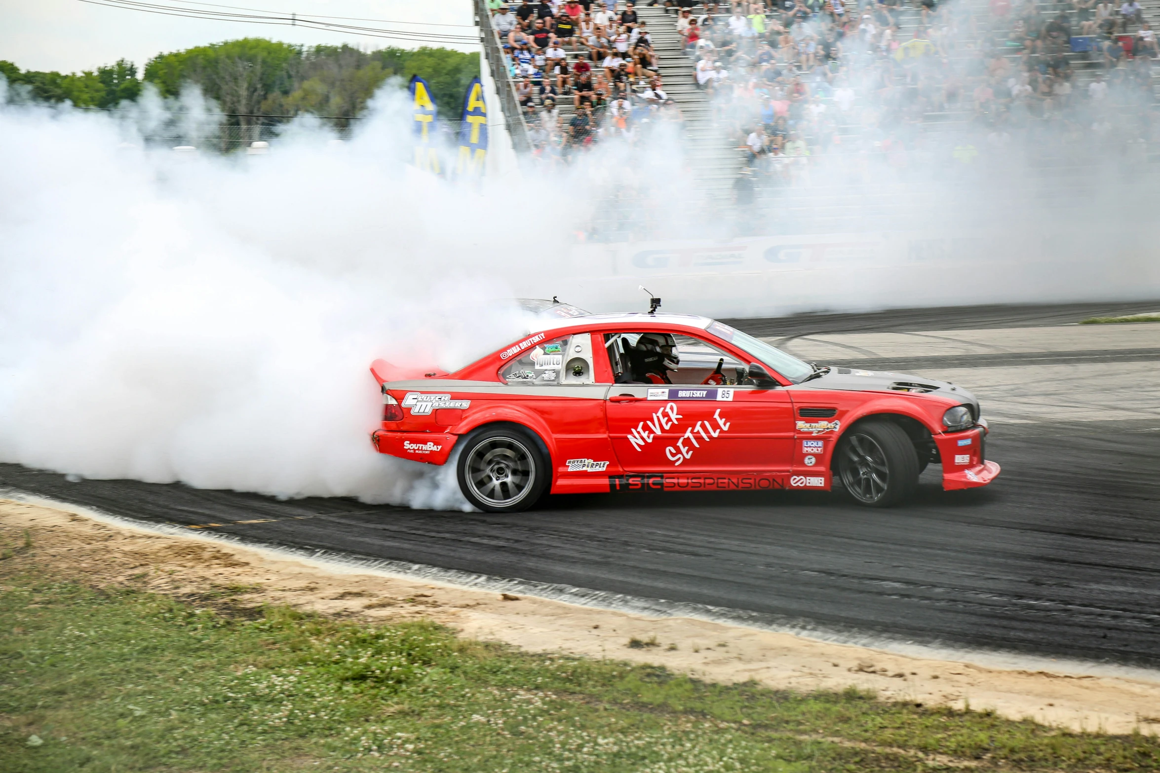 a man driving his red car on the track with a lot of smoke