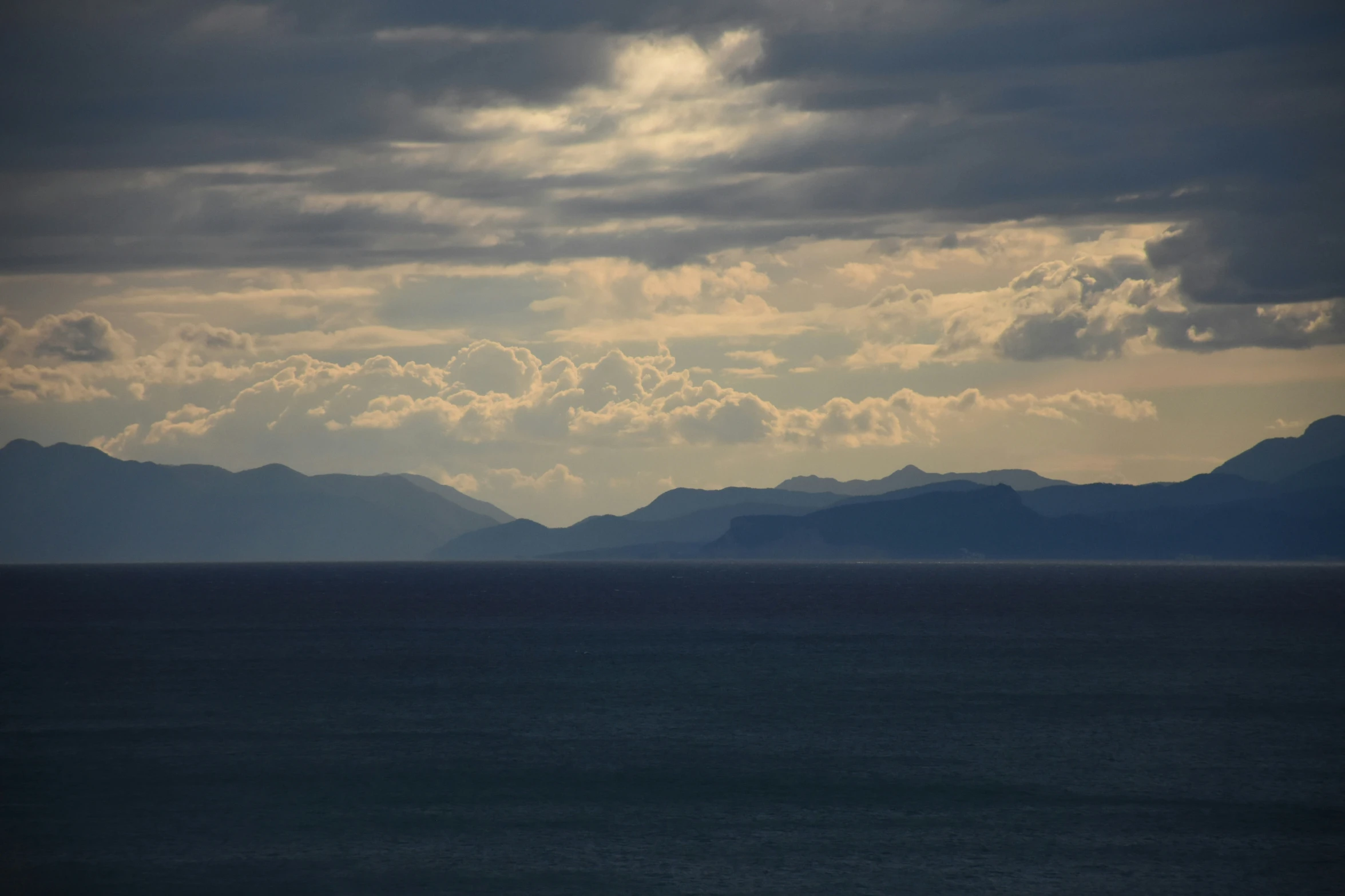some mountains and the ocean under some cloudy skies