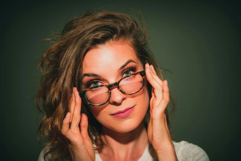 a woman in glasses posing with her hands to her ears