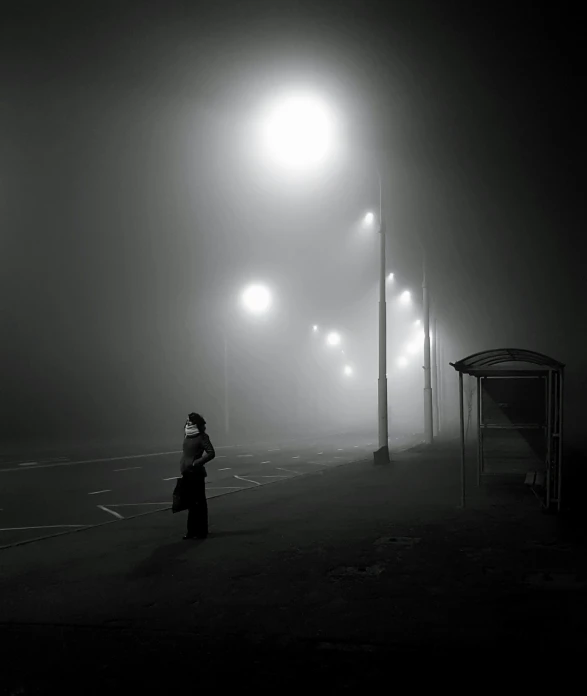 a person stands at a lighted street in the fog