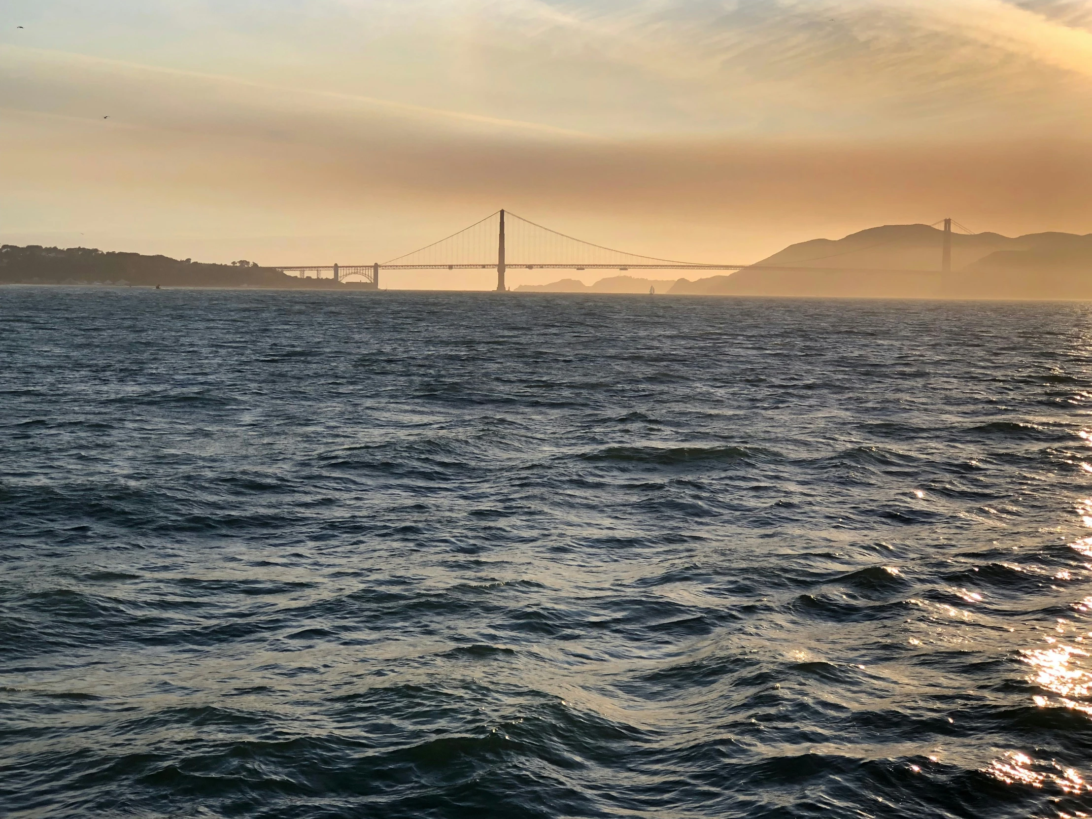 a body of water with a bridge and other hills in the distance