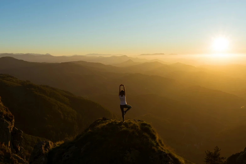 a woman standing on a mountain top in the mountains with the sun setting