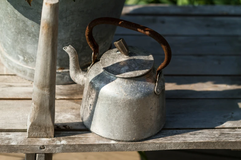 a metal tea pot and garden tools sitting on a bench