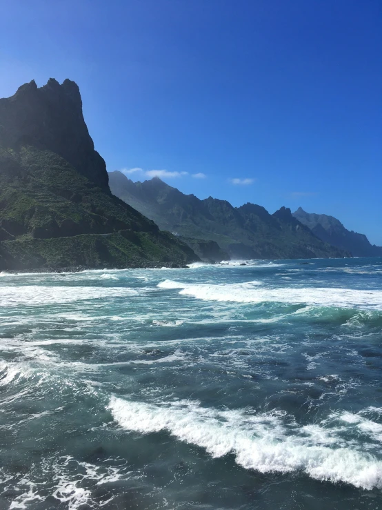 waves crashing against a mountain and beach, with sun beams