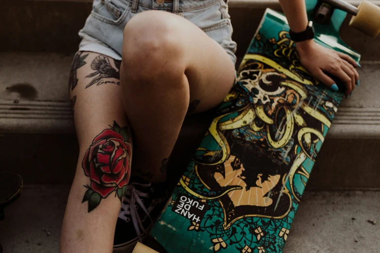 tattooed legs and arm, resting on a skateboard