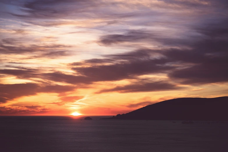 the sun is setting over the ocean by mountains