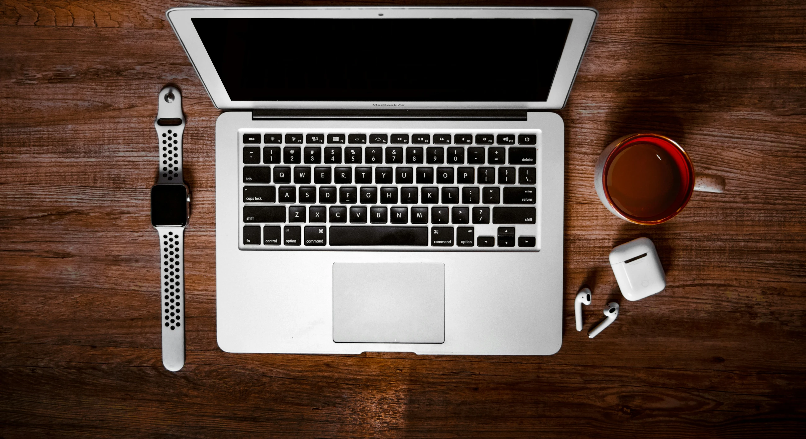 the wooden desk has a laptop, pen and charger on it