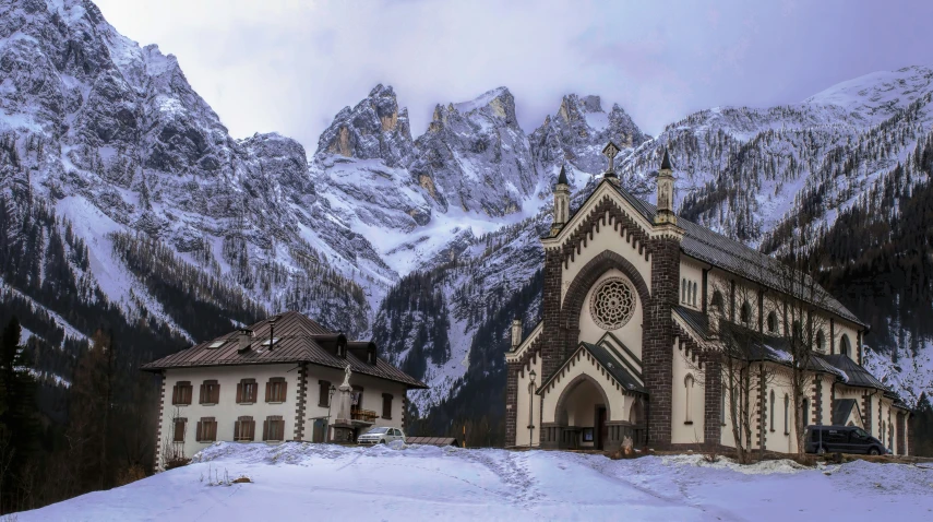 an old church sitting in the snow with mountains behind it