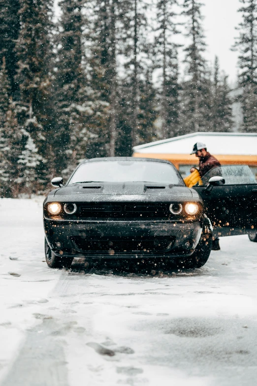 a black car is in the snow with a guy on the snow board next to it