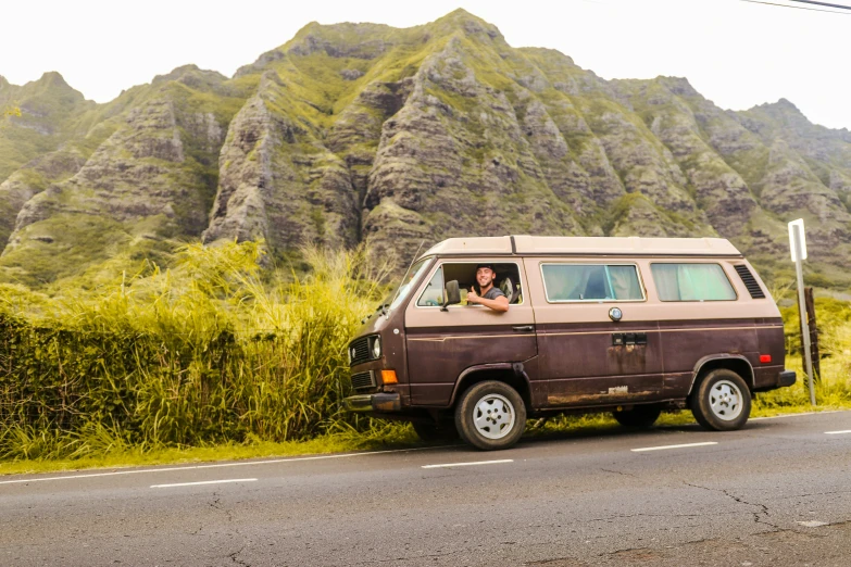 an old van drives down a street in front of a tall mountain range