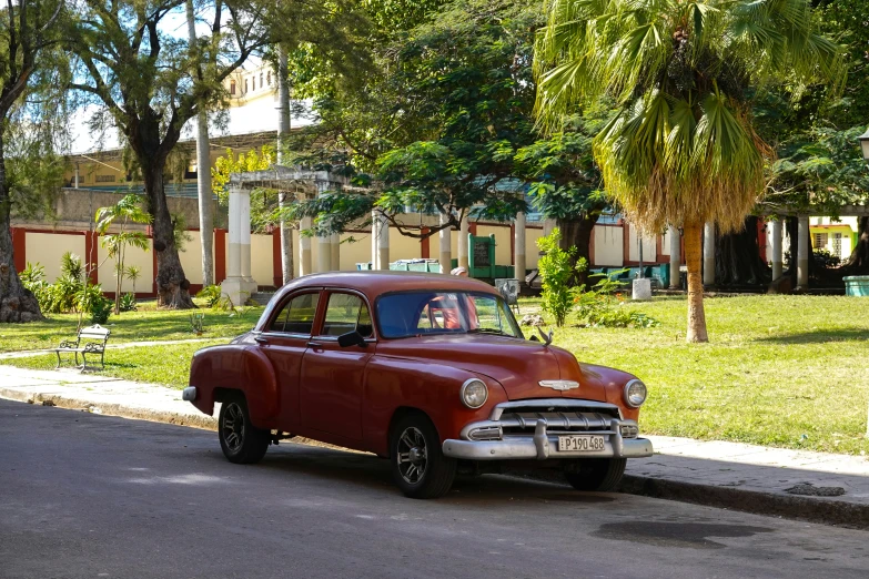 a old red and black car in street next to tree