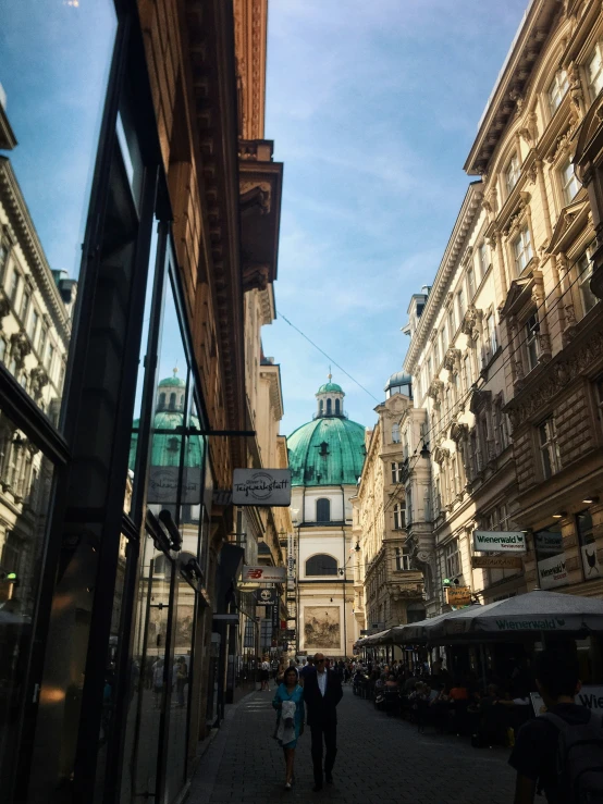 people walking past buildings with green roofs and dome tops