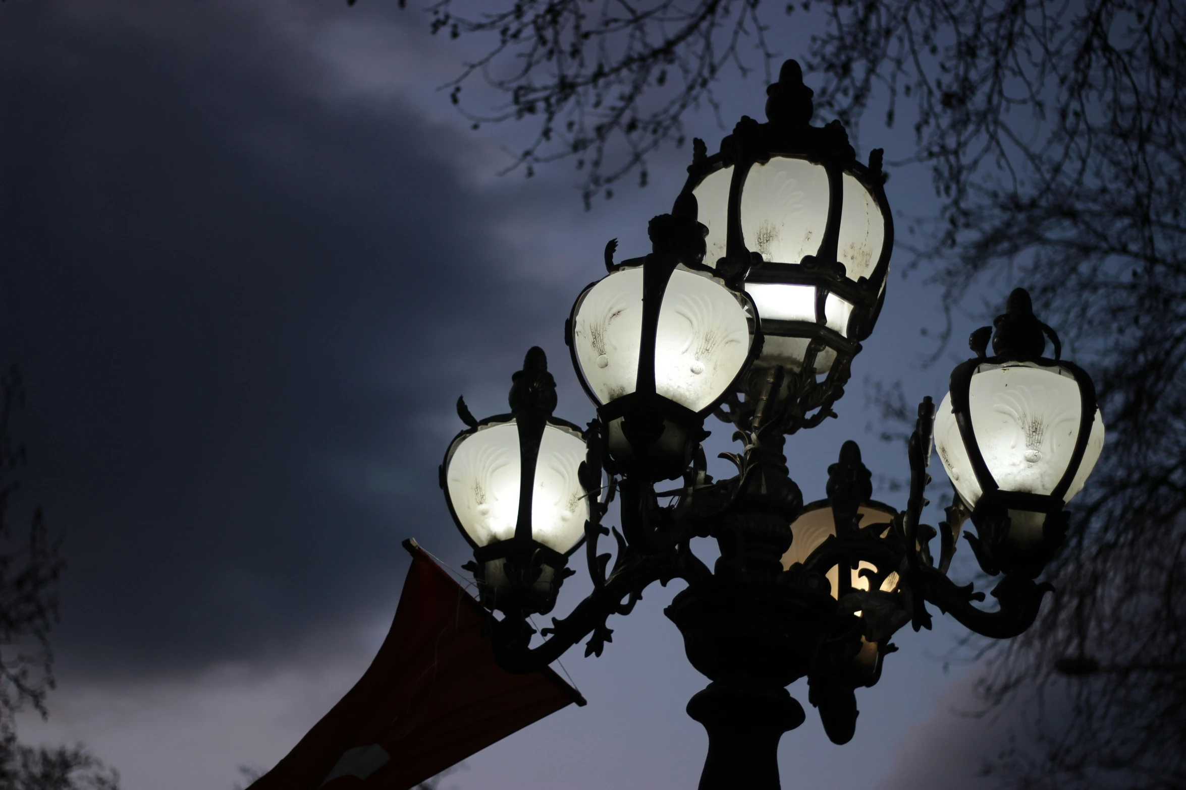 an illuminated lamp post with three flags on a cloudy night