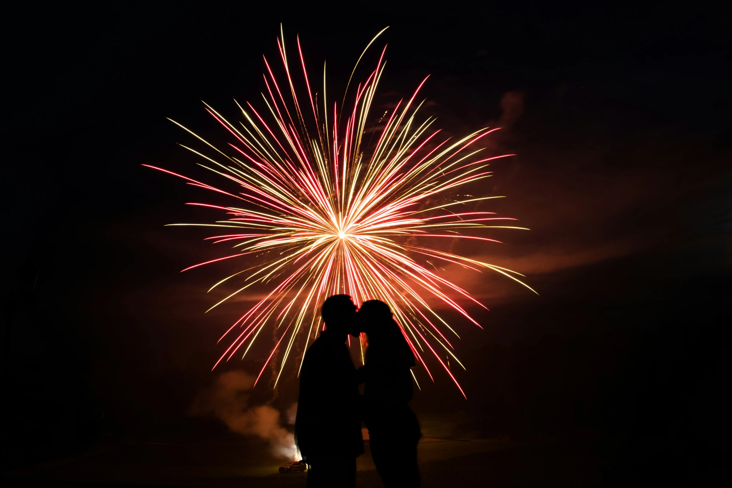 two people kissing under fireworks on a dark sky