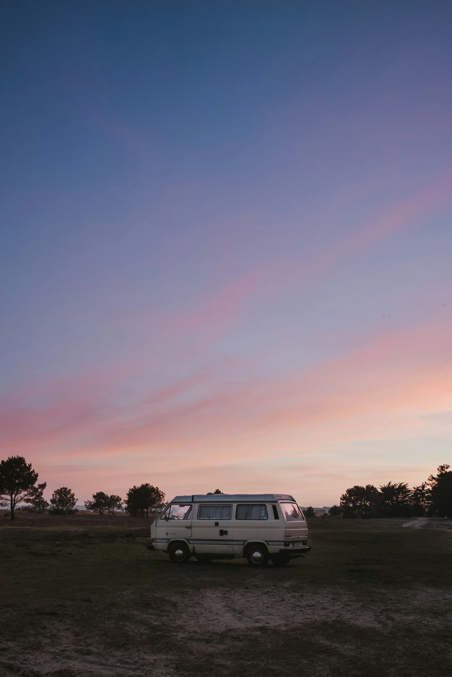 a van sits in a field beneath a pink sunset