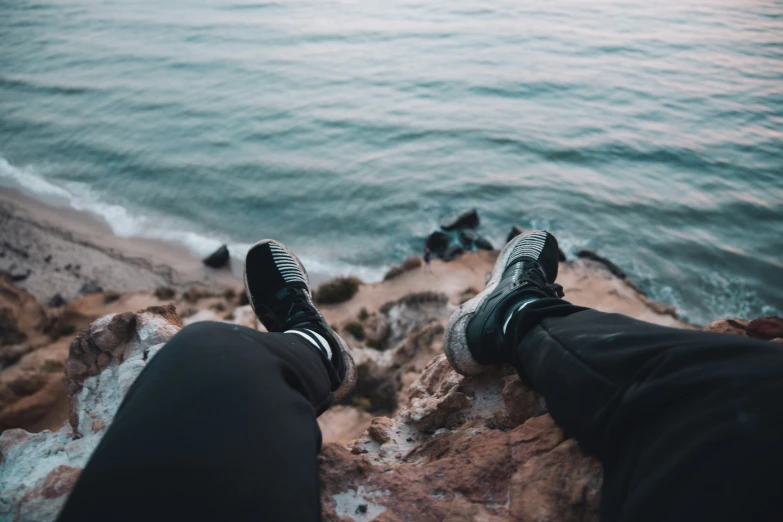 two persons are sitting on rocks overlooking a body of water